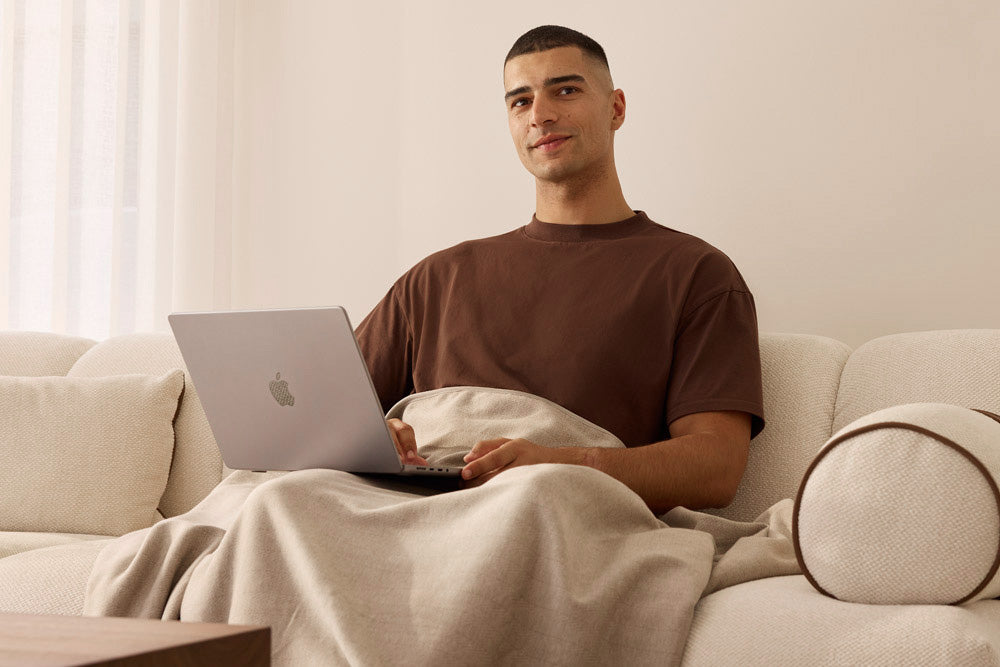 Man sitting on a couch with a laptop, wrapped in a blanket